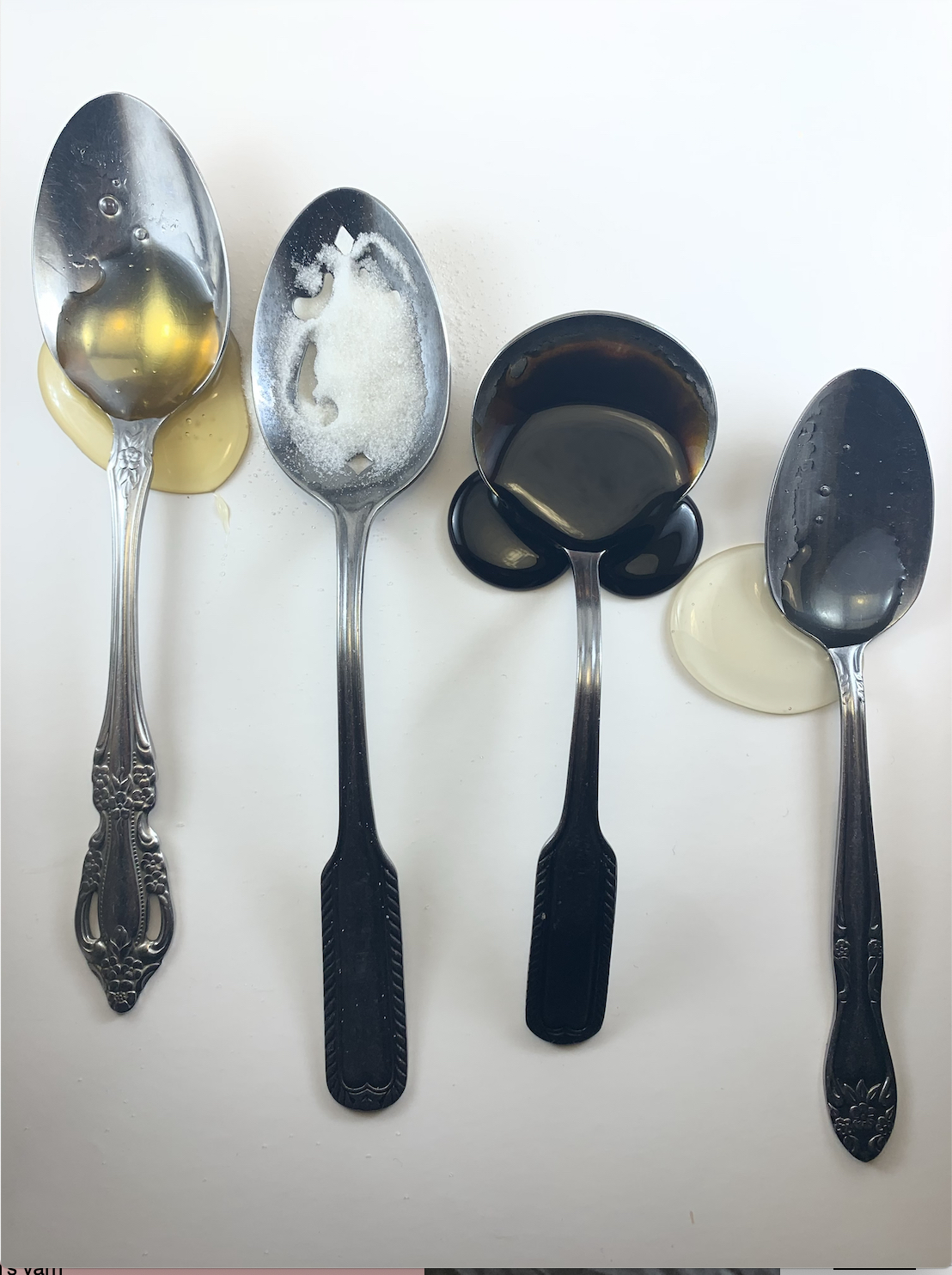 Four spoons on a white surface. Each spoon holds a different pool of liquid