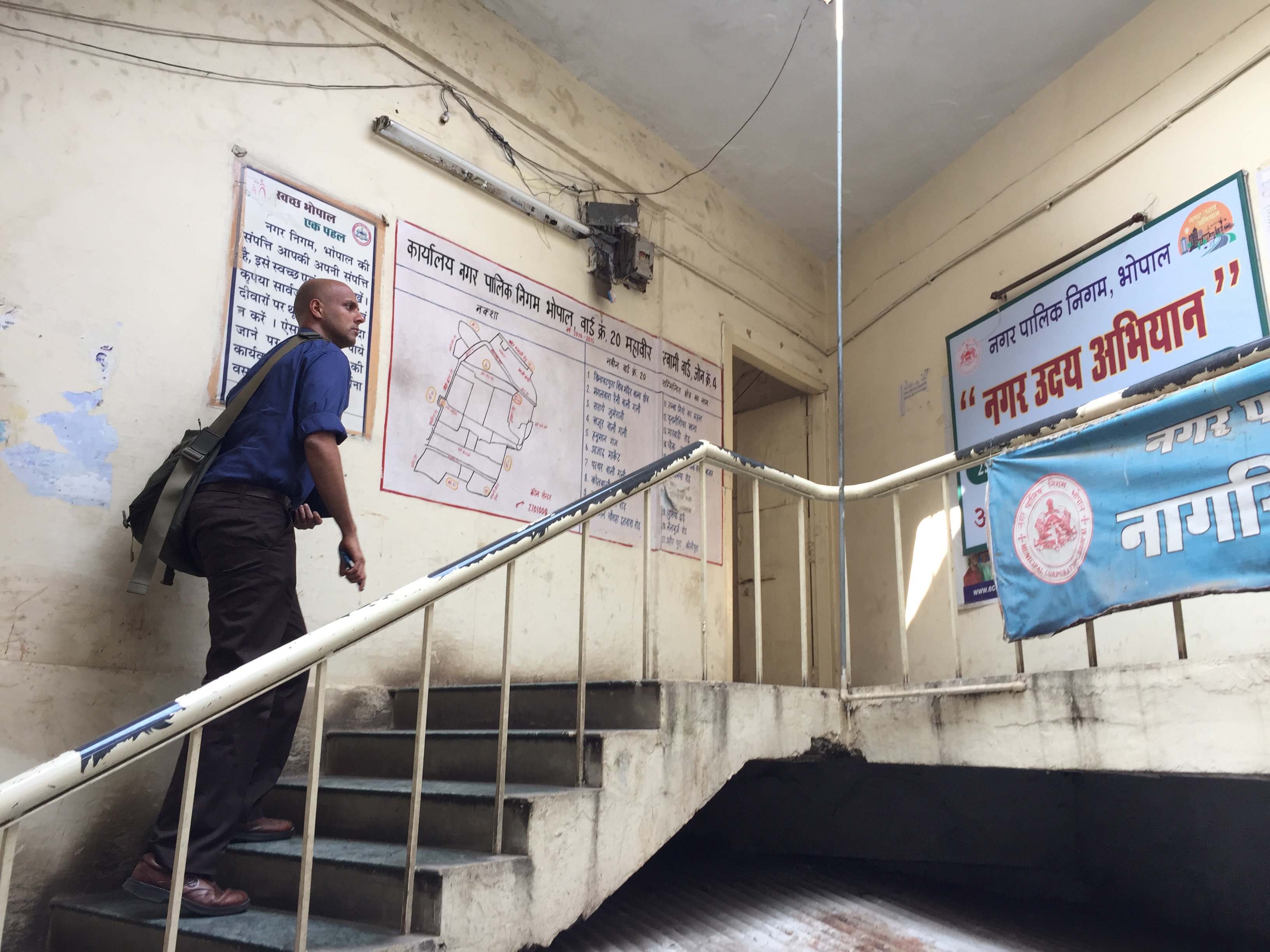 Man walks up stairs. Posters in Hindi hang on the walls. 