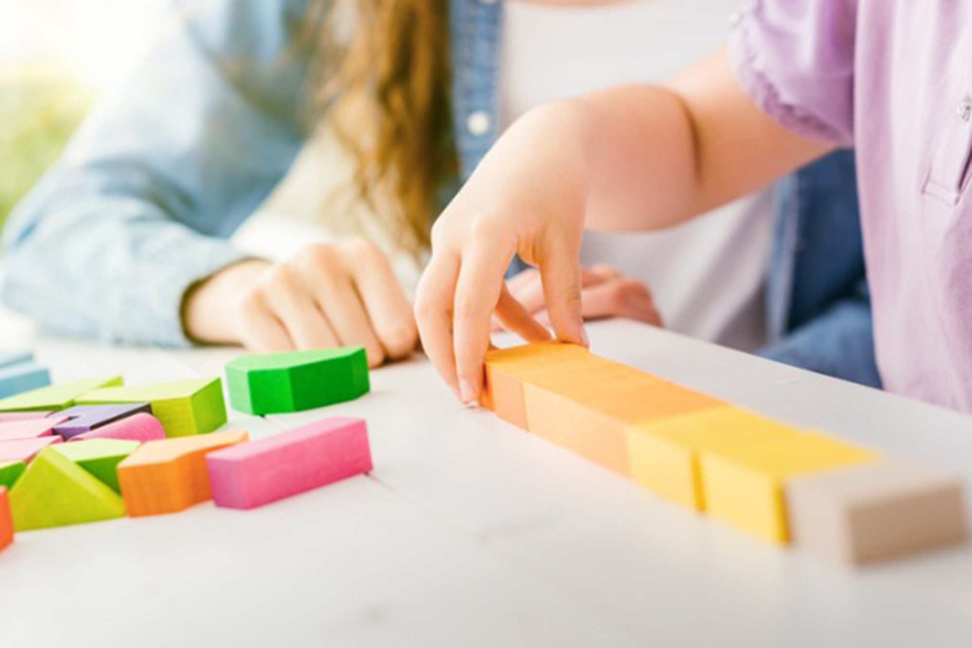 Child and caregiver playing with colorful building blocks