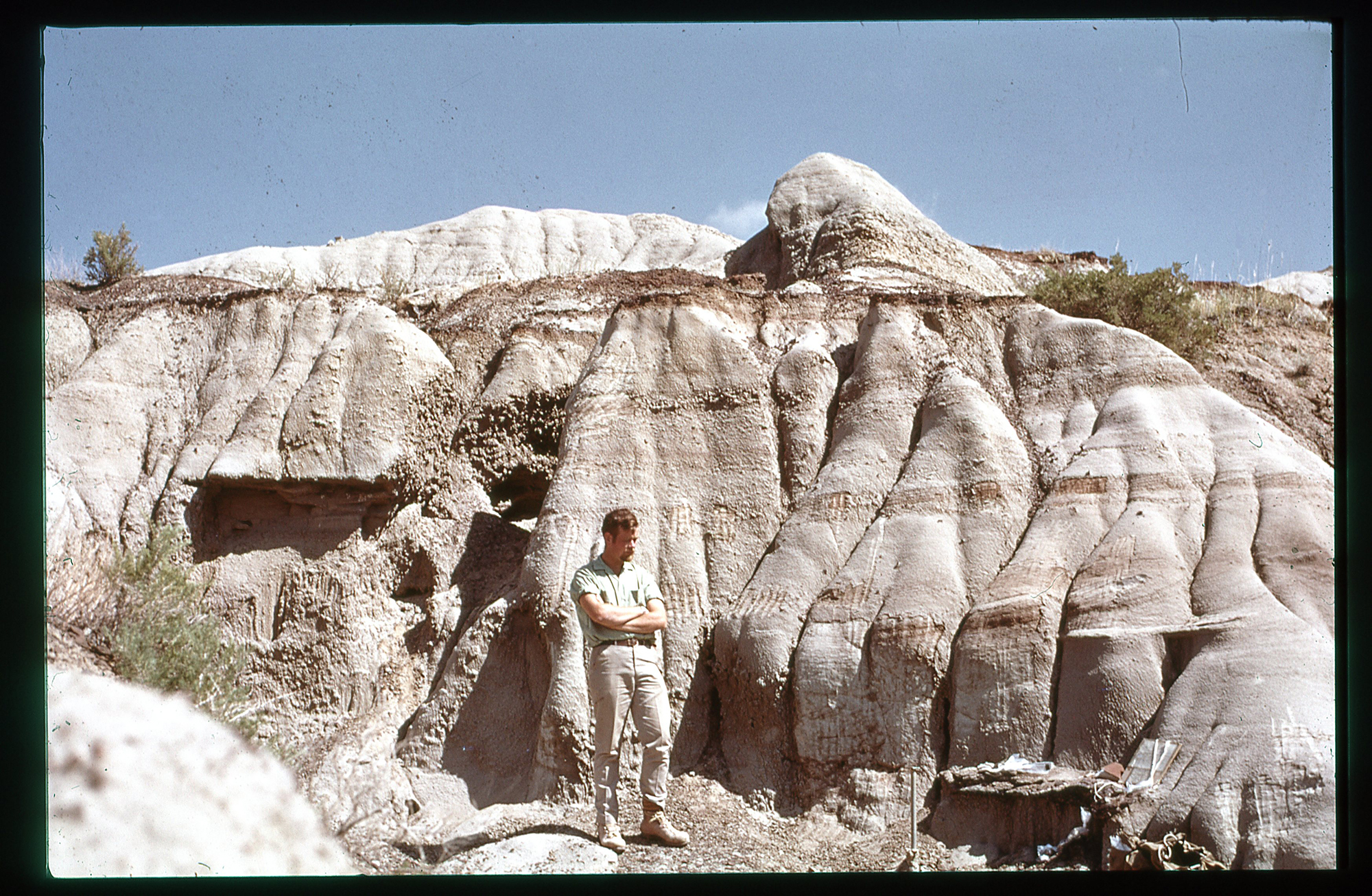 Peter Dodson in the 1960s standing with arms folded against a rock outcropping.