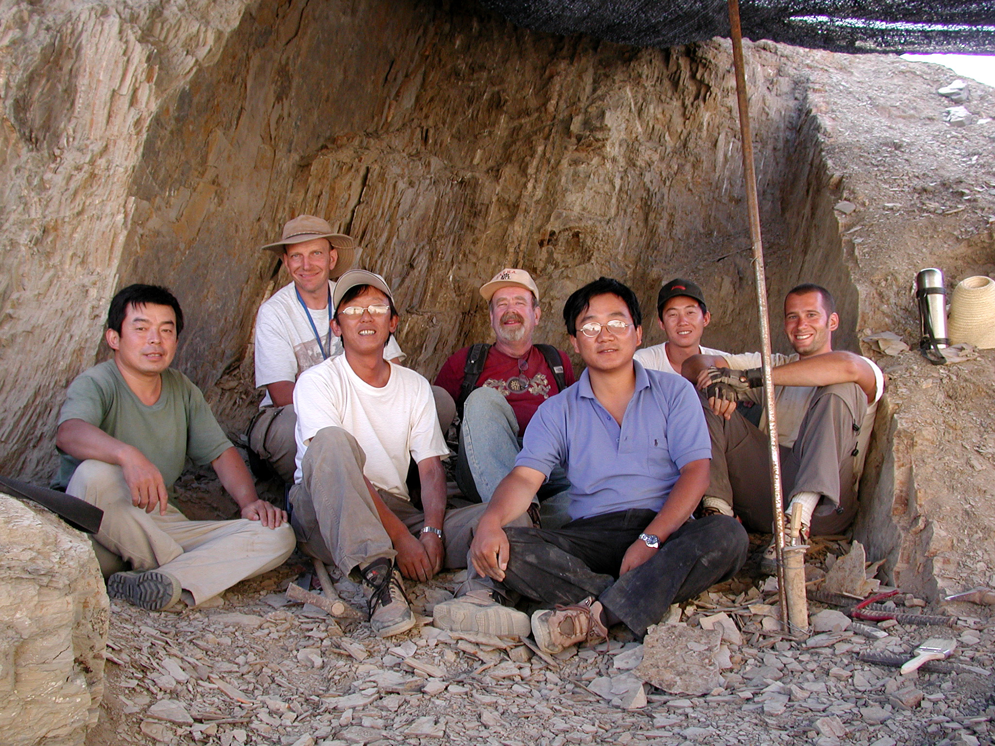Seven people sitting in an excavation cave site looking towards the camera.