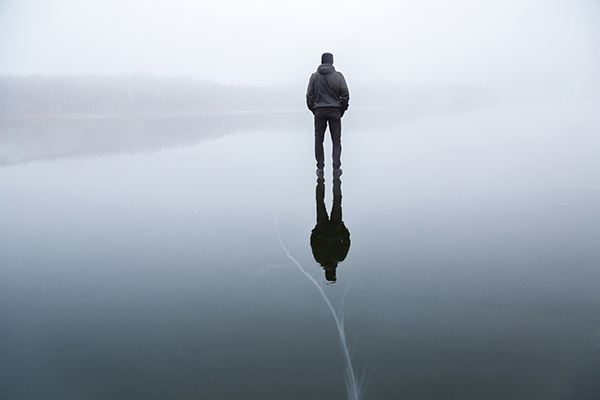 Person standing on frozen lake with back turned on a grey day.