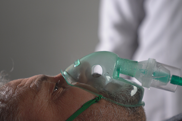 Person lying on back in hospital bed receiving oxygen via a mask.