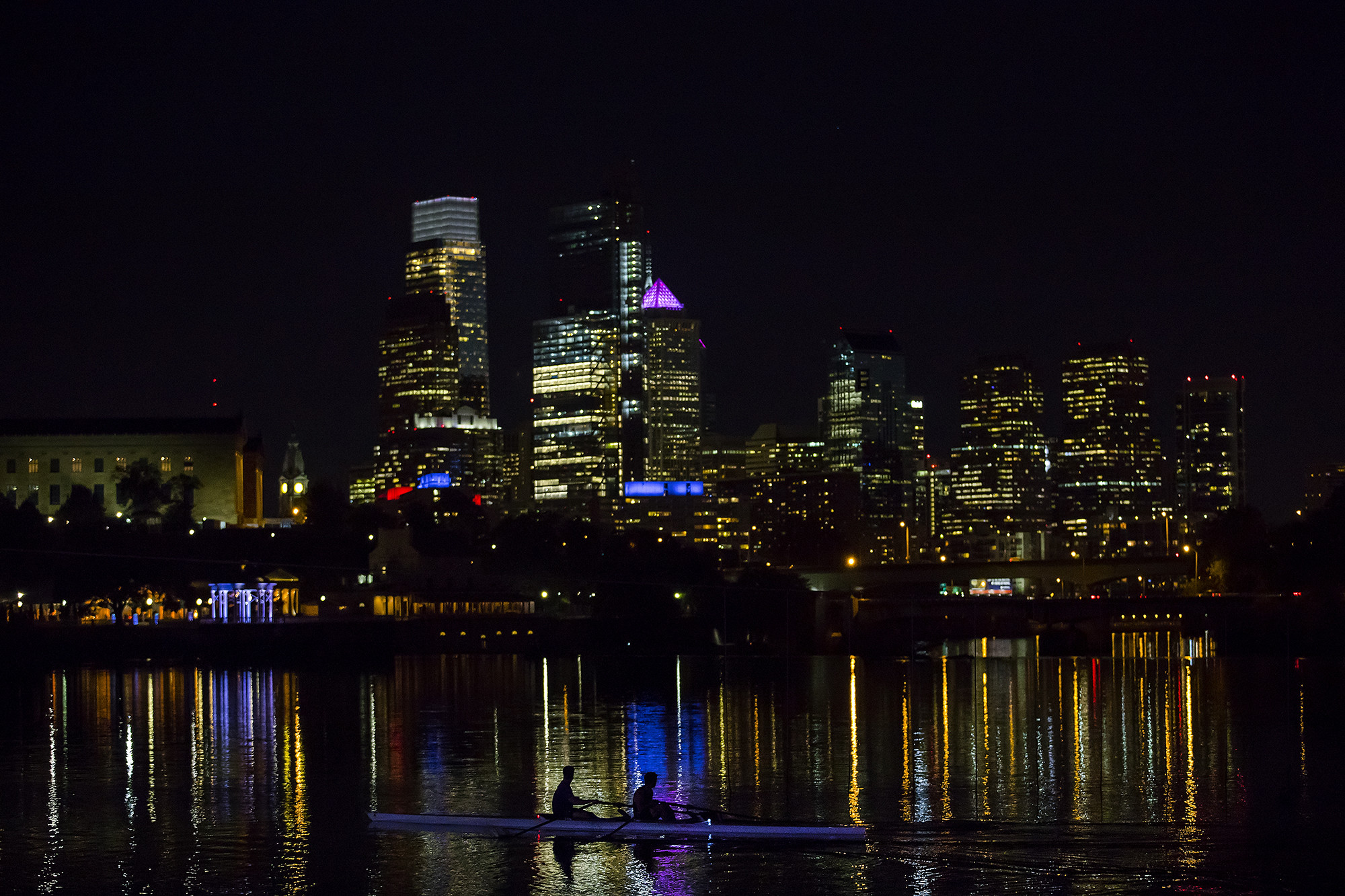 two people in a boat traveling past the philadelphia skyline at night