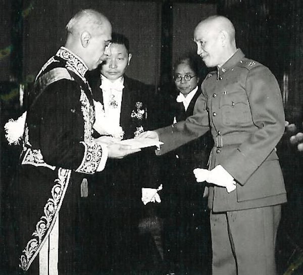 Two men shake hands and two others look on behind them in a black and white photo from the 1940s