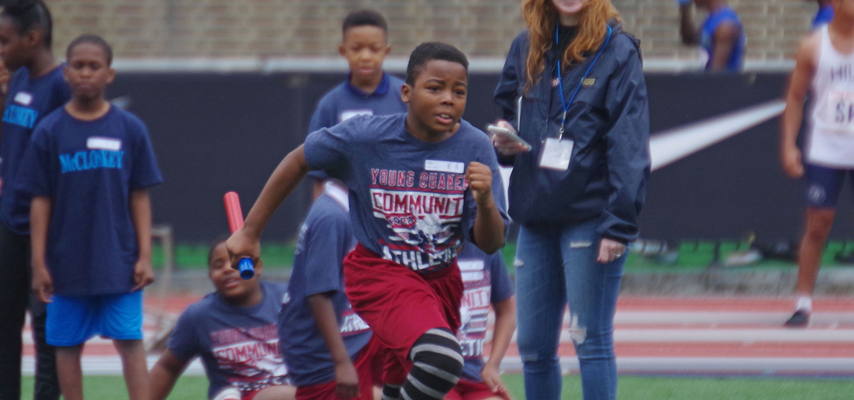 A student from West Philadelphia runs with a patron during a Young Quakers track & field event at Franklin Field.