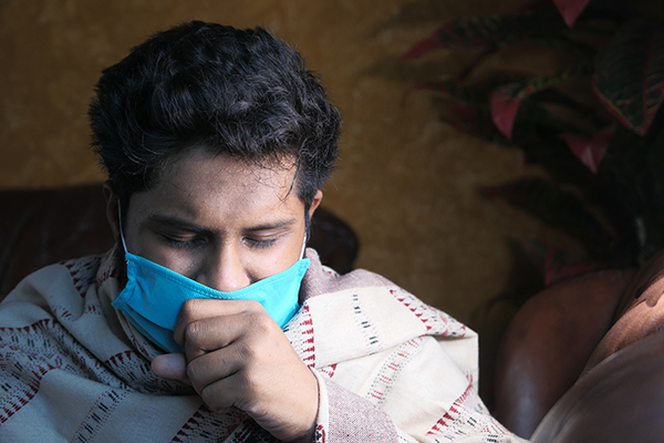Person wearing face mask and wearing a blanket coughing into fist.
