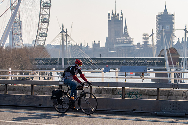 Person wearing a face mask riding a bike with the London cityscape in the background.