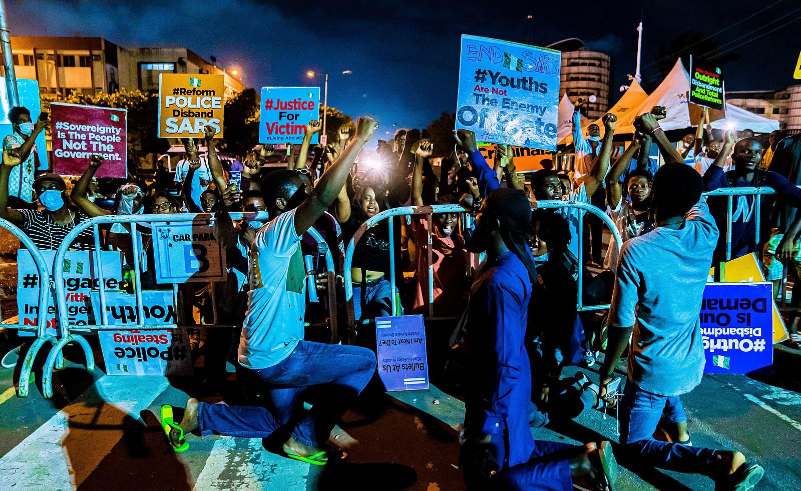 Protesters kneel in the street holding signs aloft at night