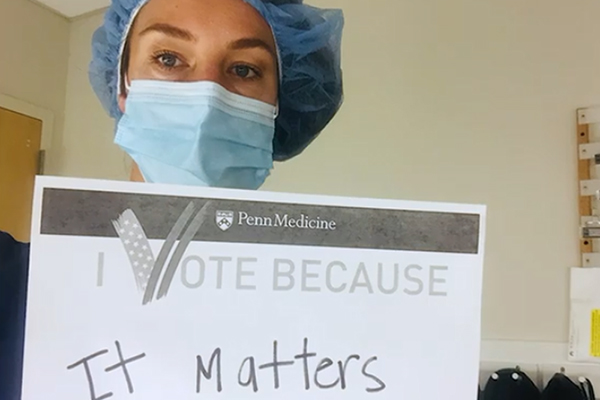 Medical worker in a cap and face mask holding up a sign that reads I Vote Because It Matters.