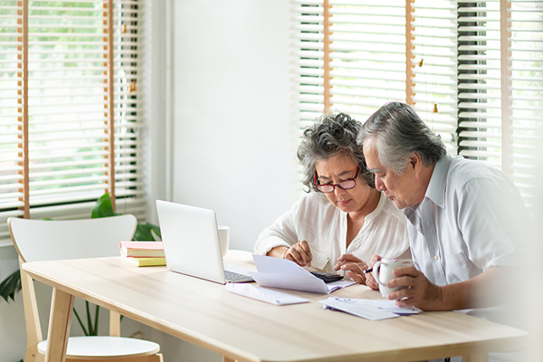 Aging couple looking at financial papers and a laptop with concern at a kitchen table.