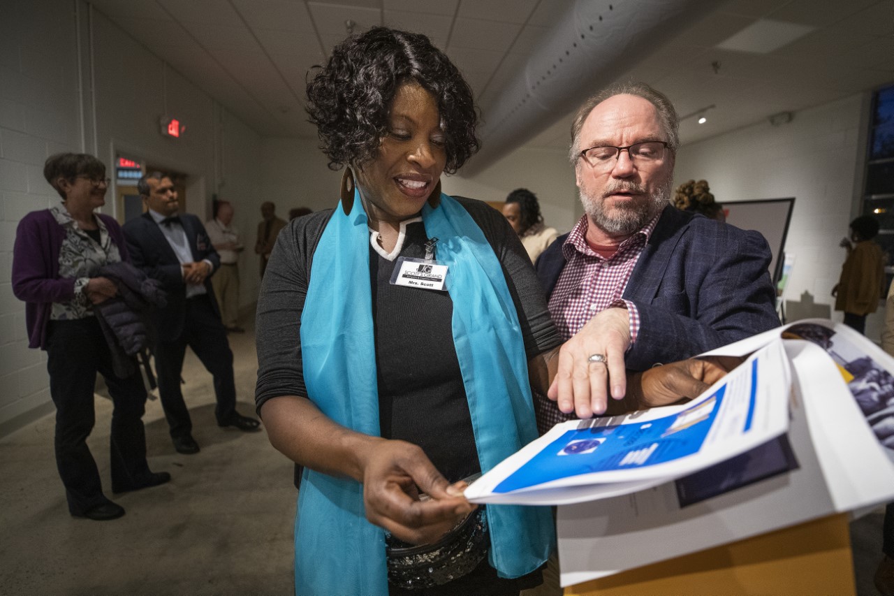 Two people looking at documents, with one person explaining them to the other. More people stand in the background.