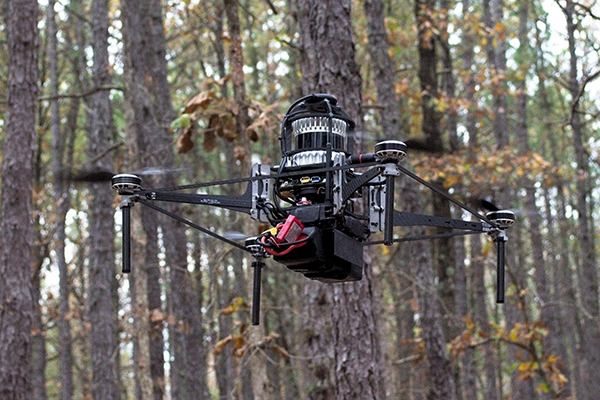 A flying robot flying in a forest in daylight.