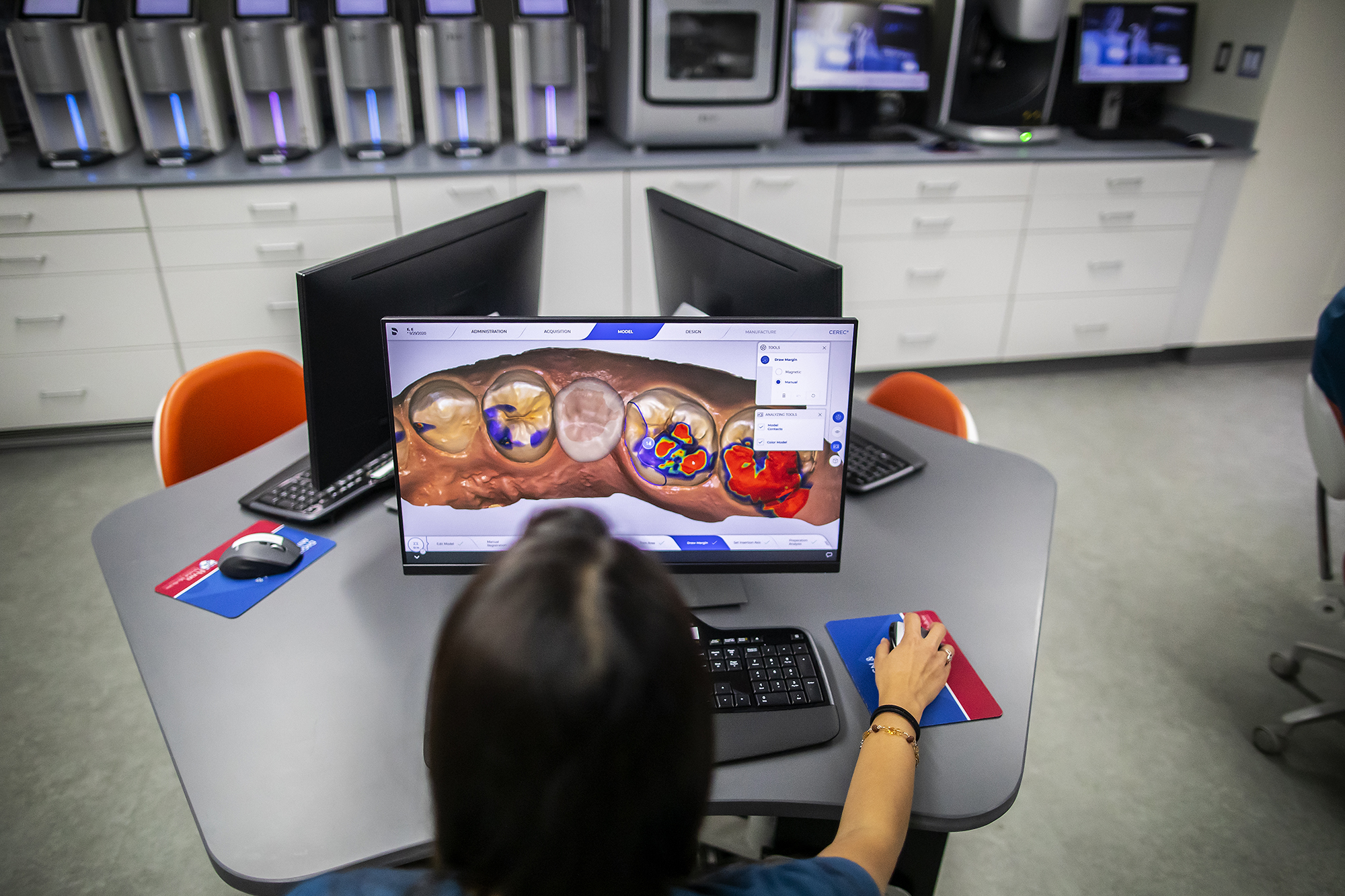 A person sits at a computer looking at a microscopic view of mouth anatomy on screen.