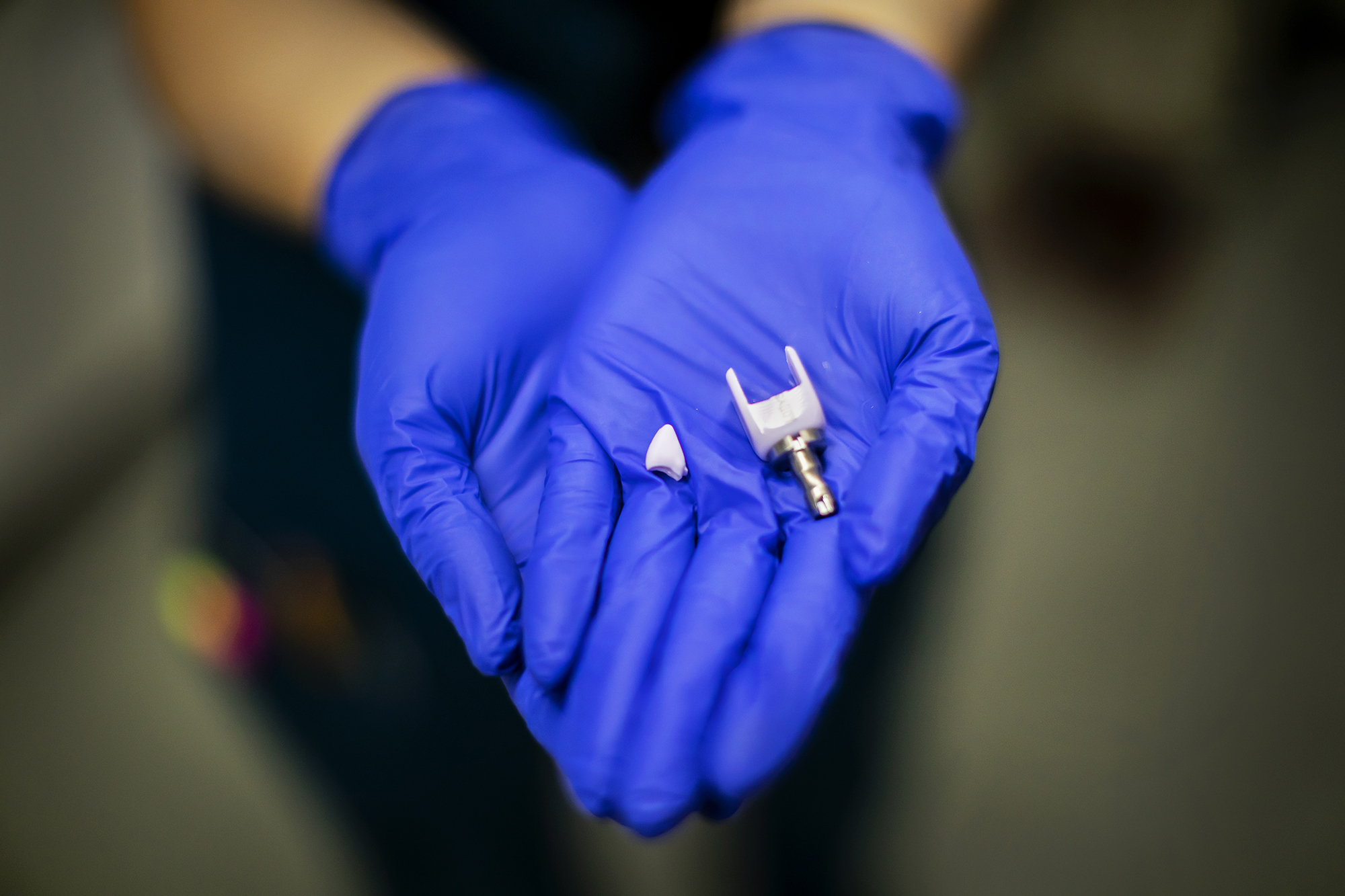 A pair of gloved hands holding a high-tech ceramic tooth model.