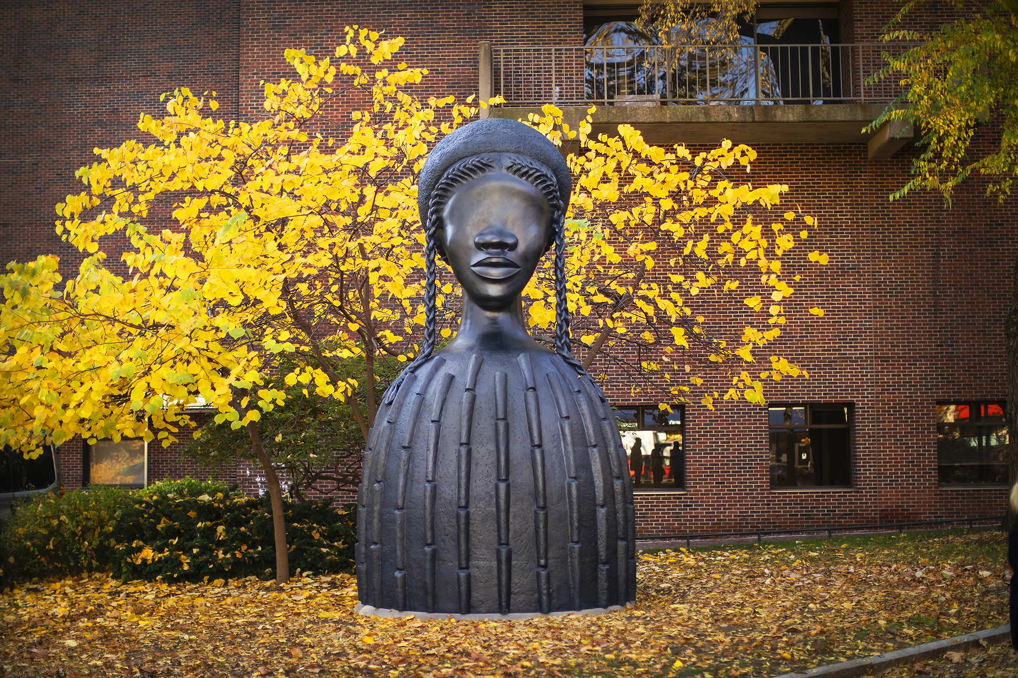 Bronze sculpture of a large bust of a Black woman on Penn’s campus surrounded by autumn leaves