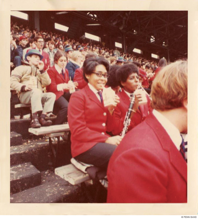 Two members of the Penn Band sitting in the stands drinking from straws.