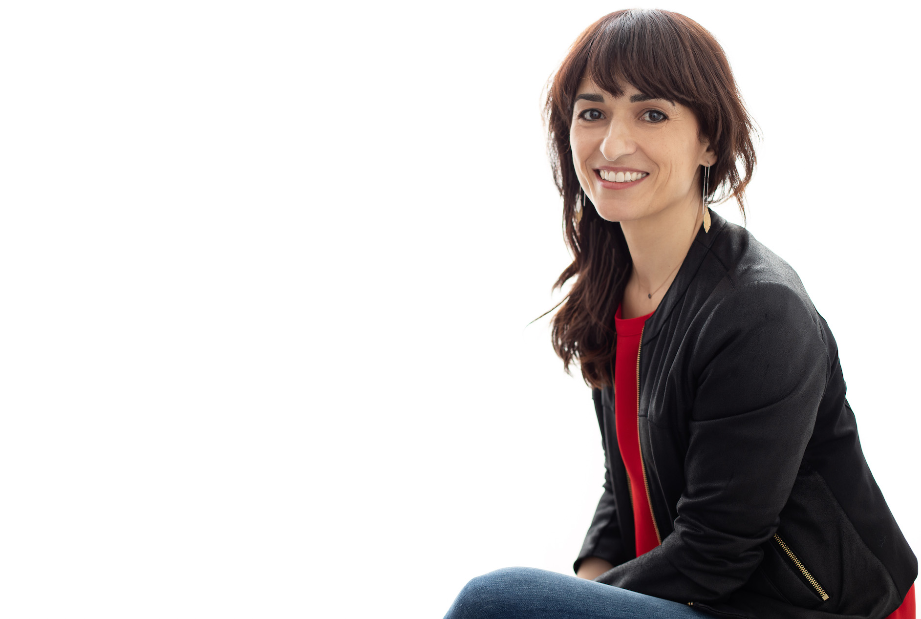 Person sitting, sideways facing the camera, smiling, on a white background. 