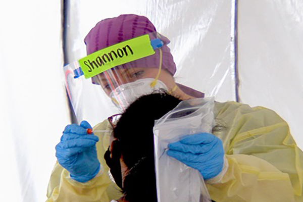 A person in full PPE is administering a COVID nasal swab test.