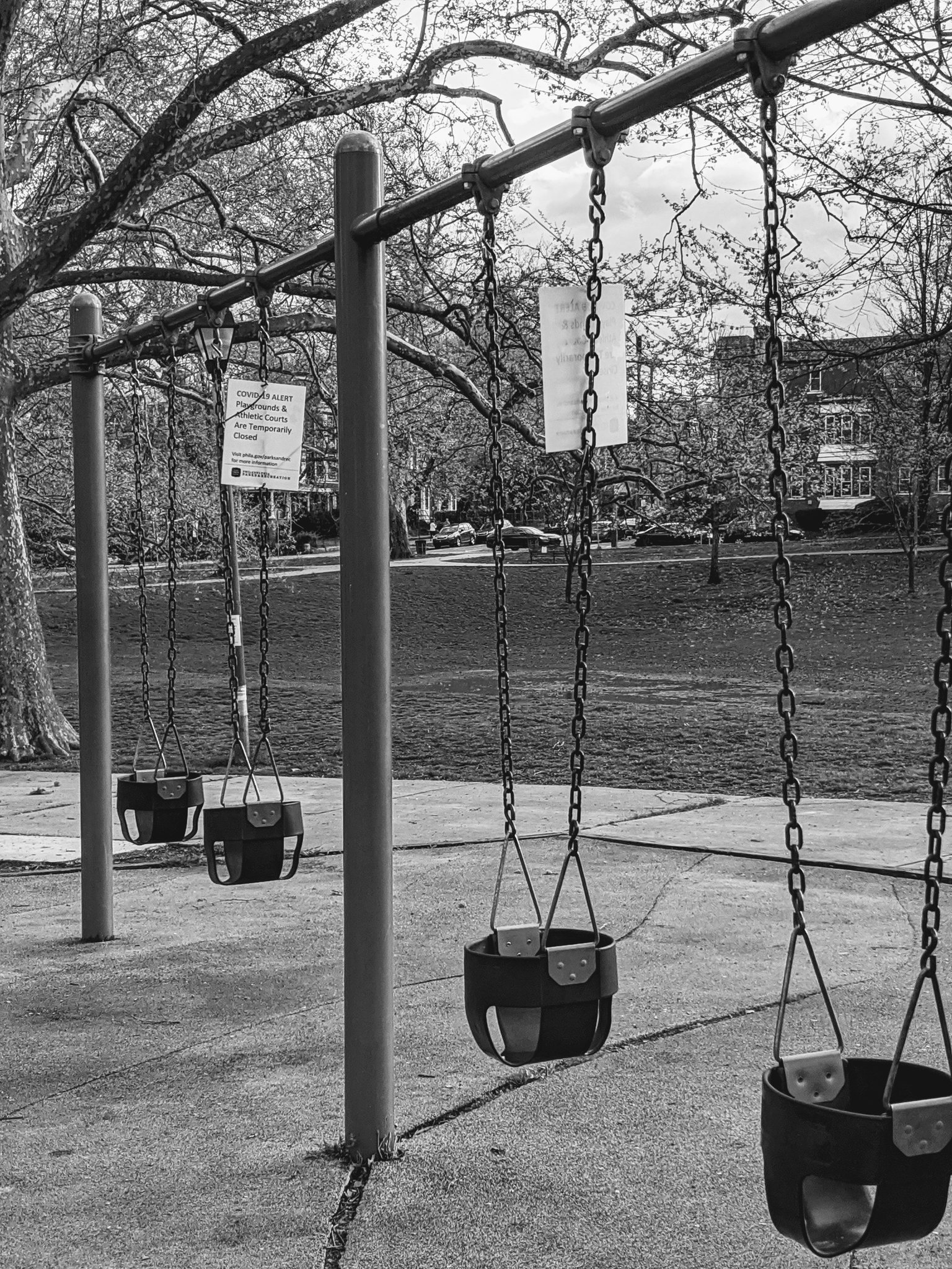 Park swings at a playground sit empty with a posted coronavirus warning sign indicating the park is closed.