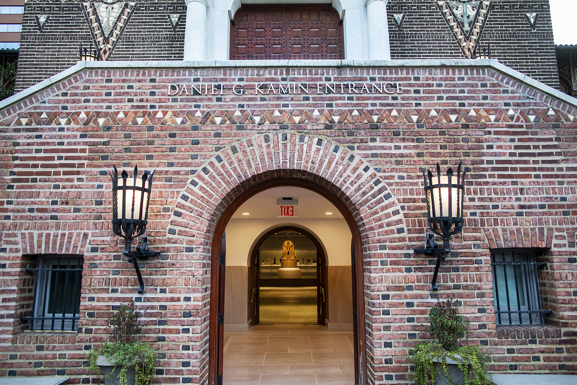 Main entrance of Penn Museum with brick wall and door open showing arched passageway with Sphinx in the doorway in the very back of the view.