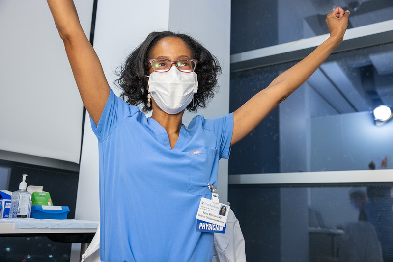 A person in scrubs and a mask with arms in the air in celebration. A tag hanging from the scrubs reads "Physician."