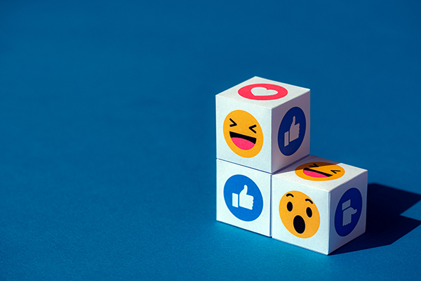 Three cubes with Facebook messenger emojis printed on each side displaying the trademark thumb’s up, the laugh emoji and the surprise emoji.