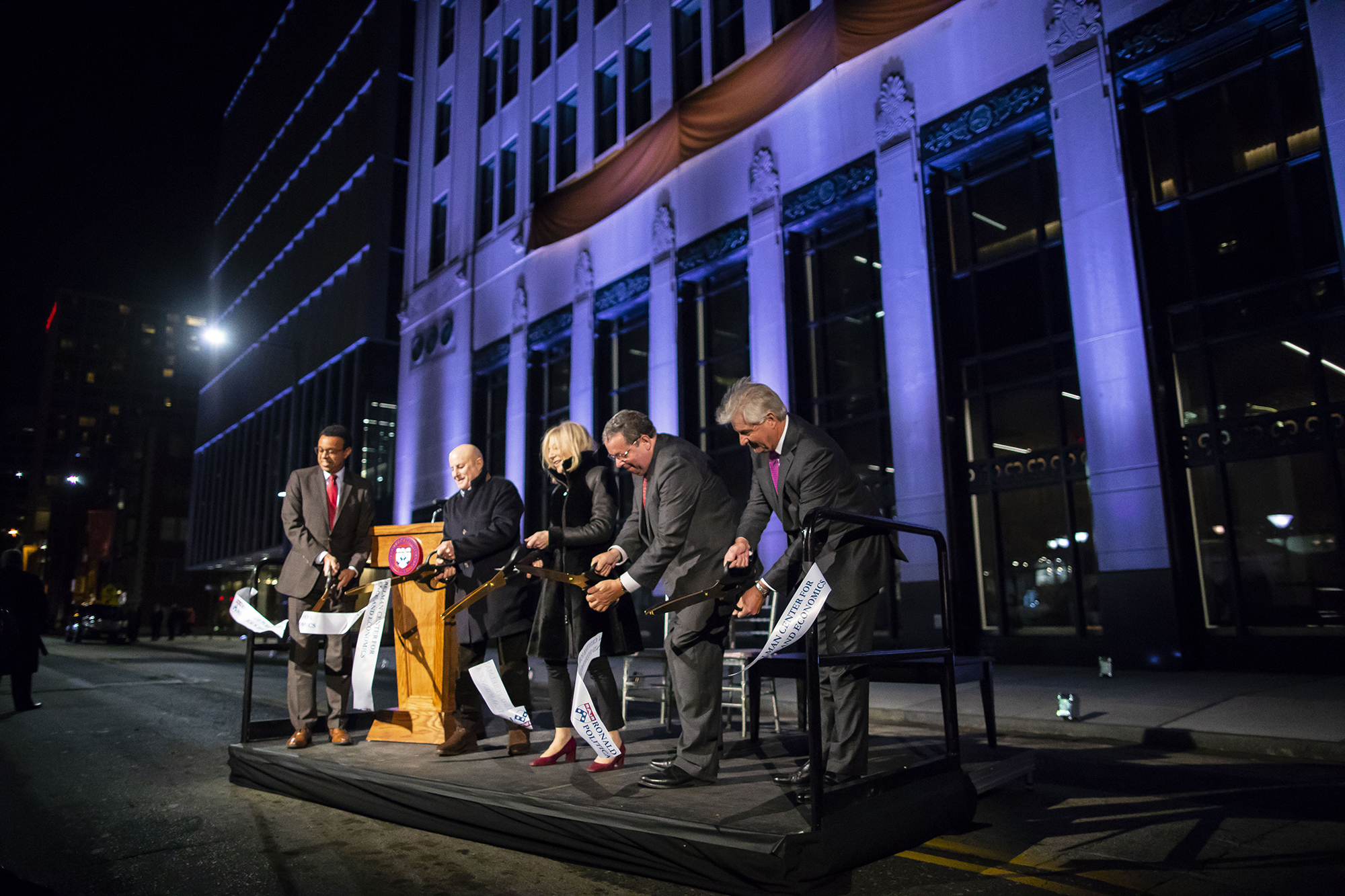 Five people, including Wendell Pritchett, Steve Fluharty, and Amy Gutann, cut a ribbon on a small platform with a podium in front of the new Perelman building.