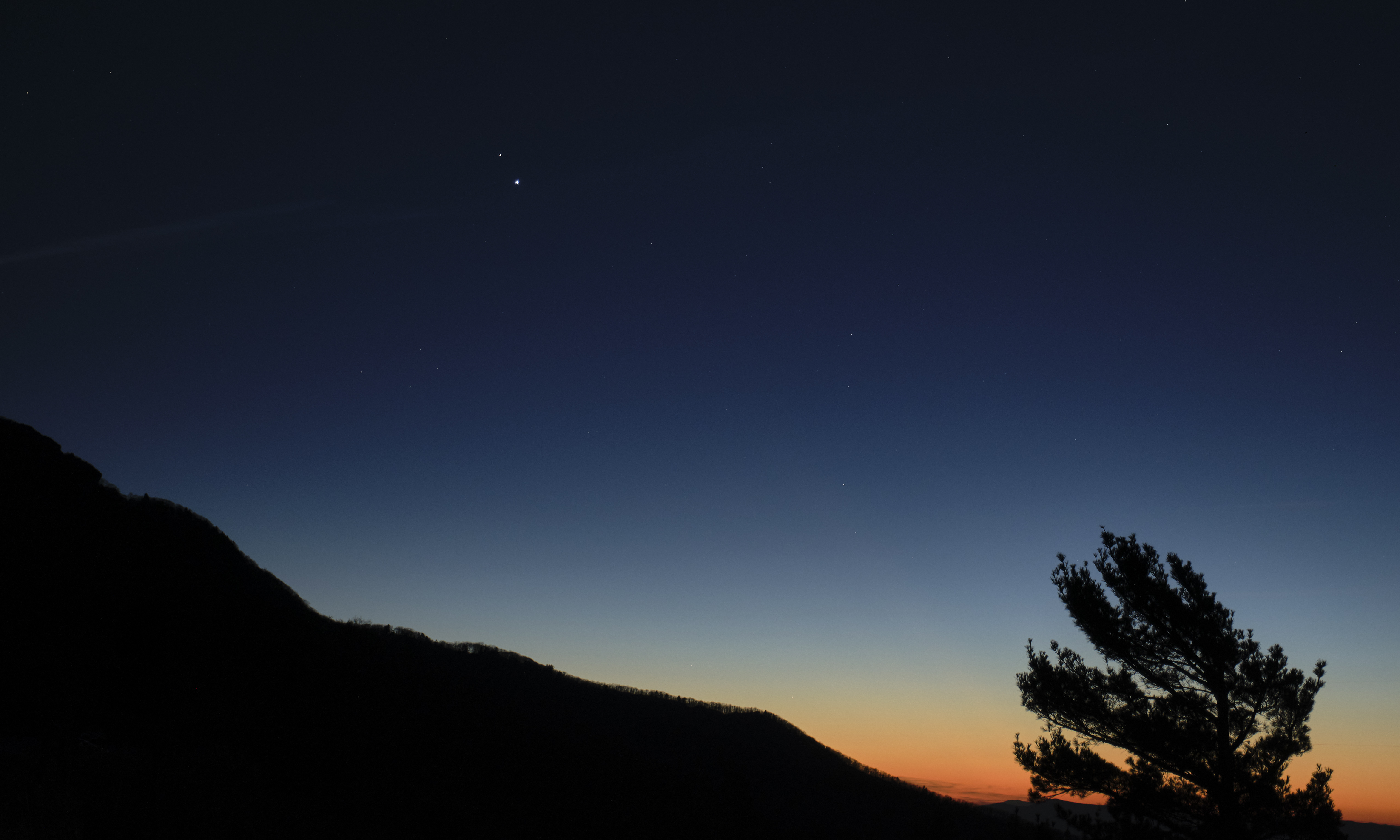 jupiter and saturn visible at dusk just above the horizon of a dark mountain landscape
