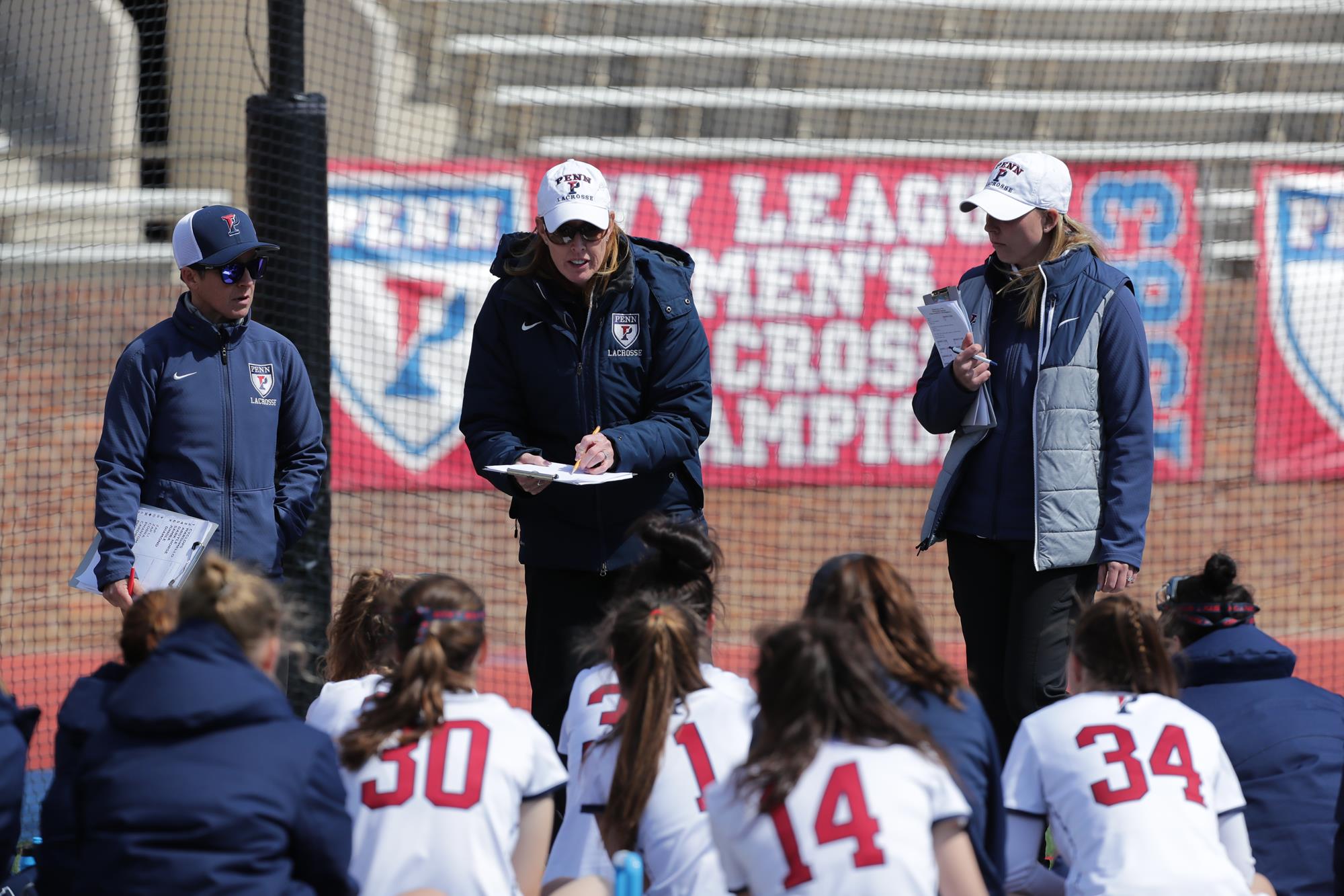 Coach Corbett speaks to her players, who are huddled on the ground in front of her.