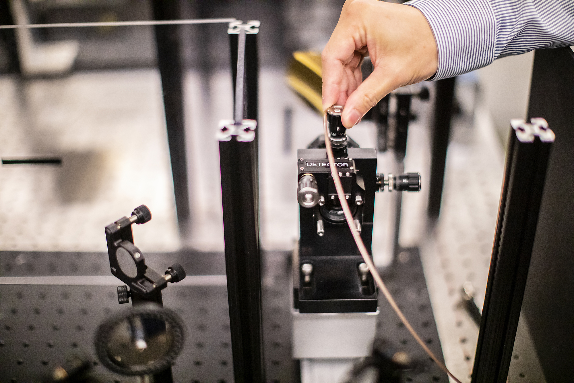 a hand adjusting a lens on an optics table