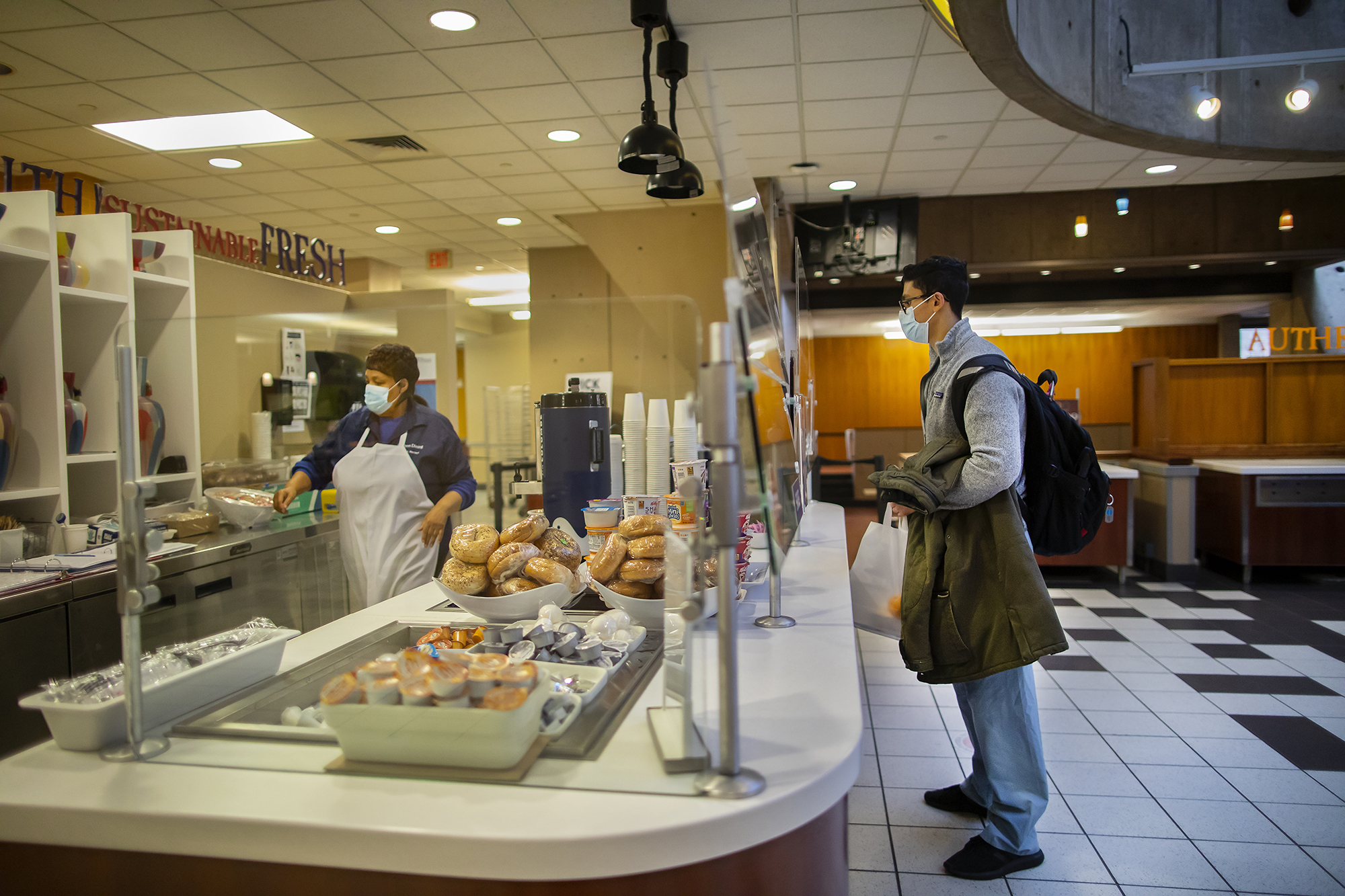 A student wearing a mask orders food from a food service worker wearing a mask at a Penn Dining location.