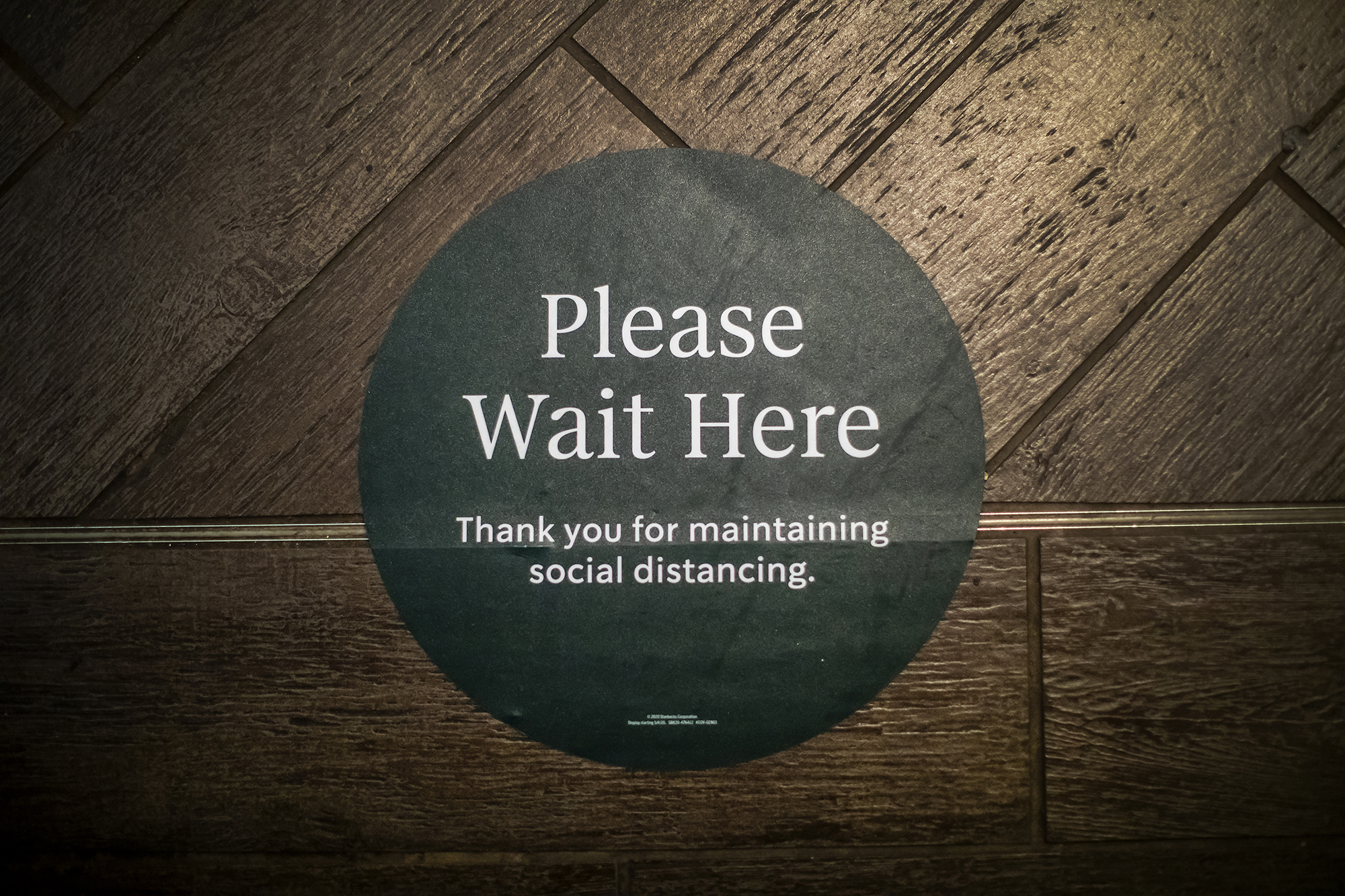 Decal on wall that reads Please Wait Here Thank you for maintaining social distance.