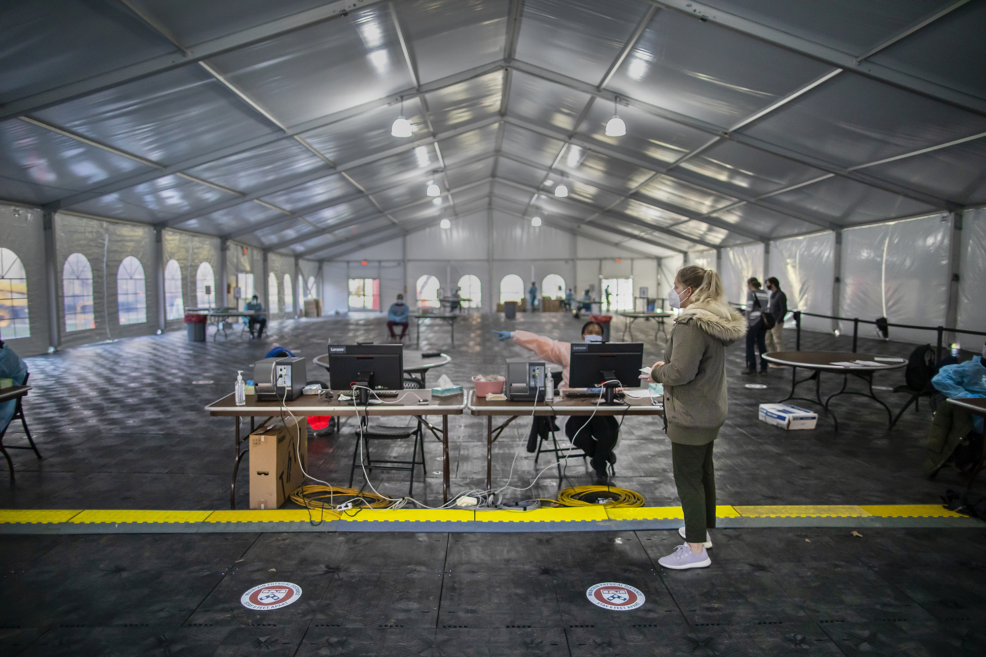 a person standing in front of a desk receiving instructions on where to go inside of a tent for covid testing