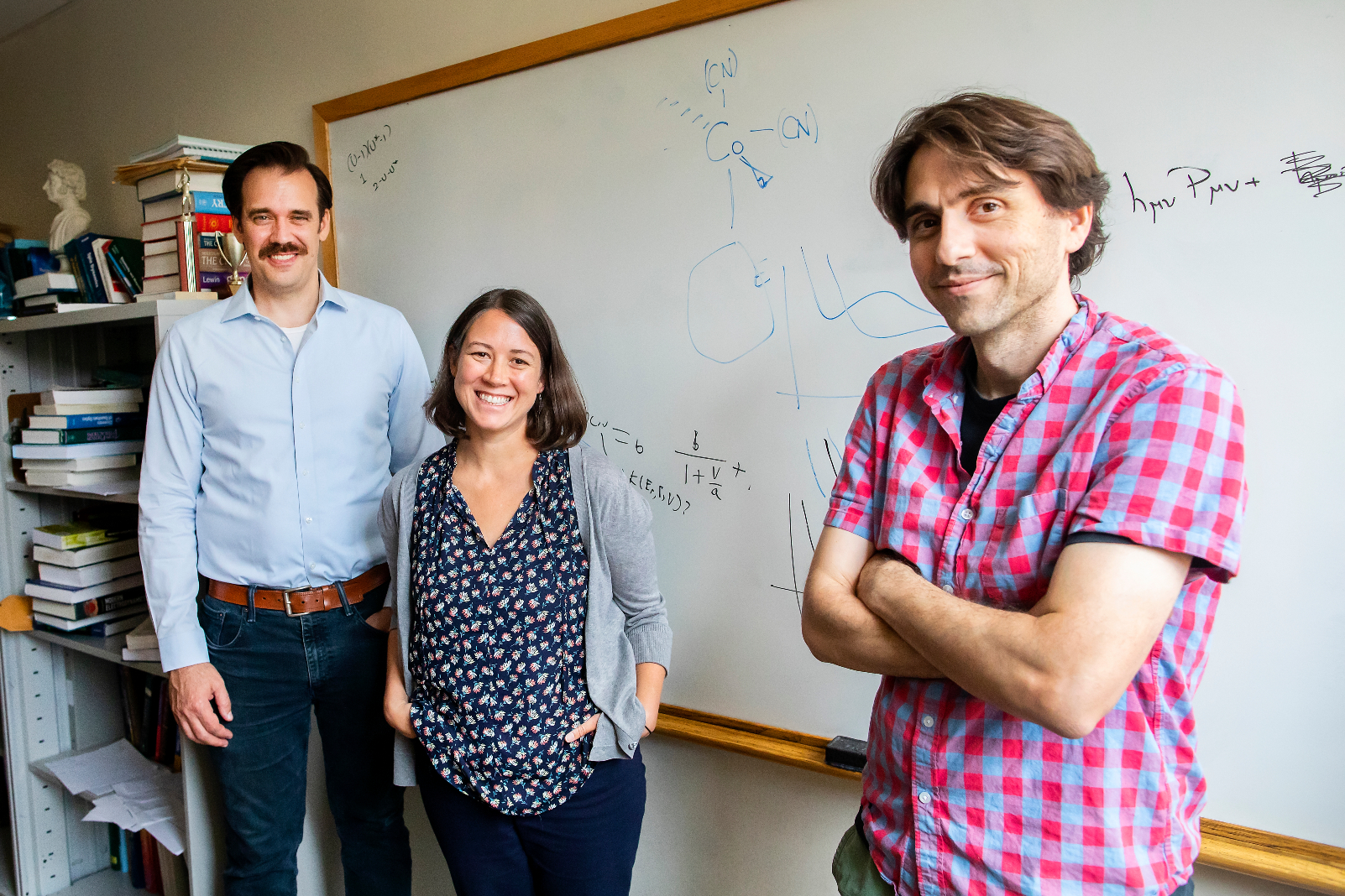 three people in front of a white board with equations and chemical formulas