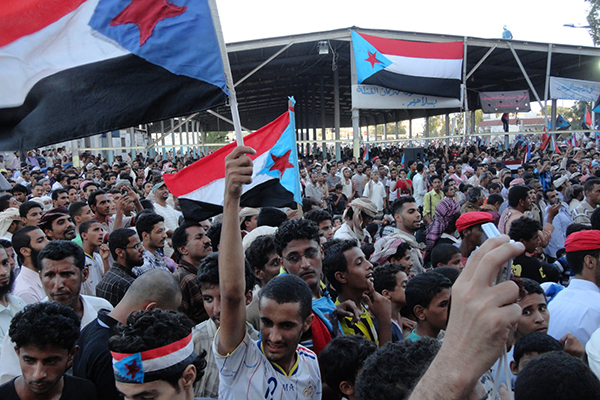 Large group of men gather in the street in Yemen holding the country's flag during the 2011 Arab Spring.