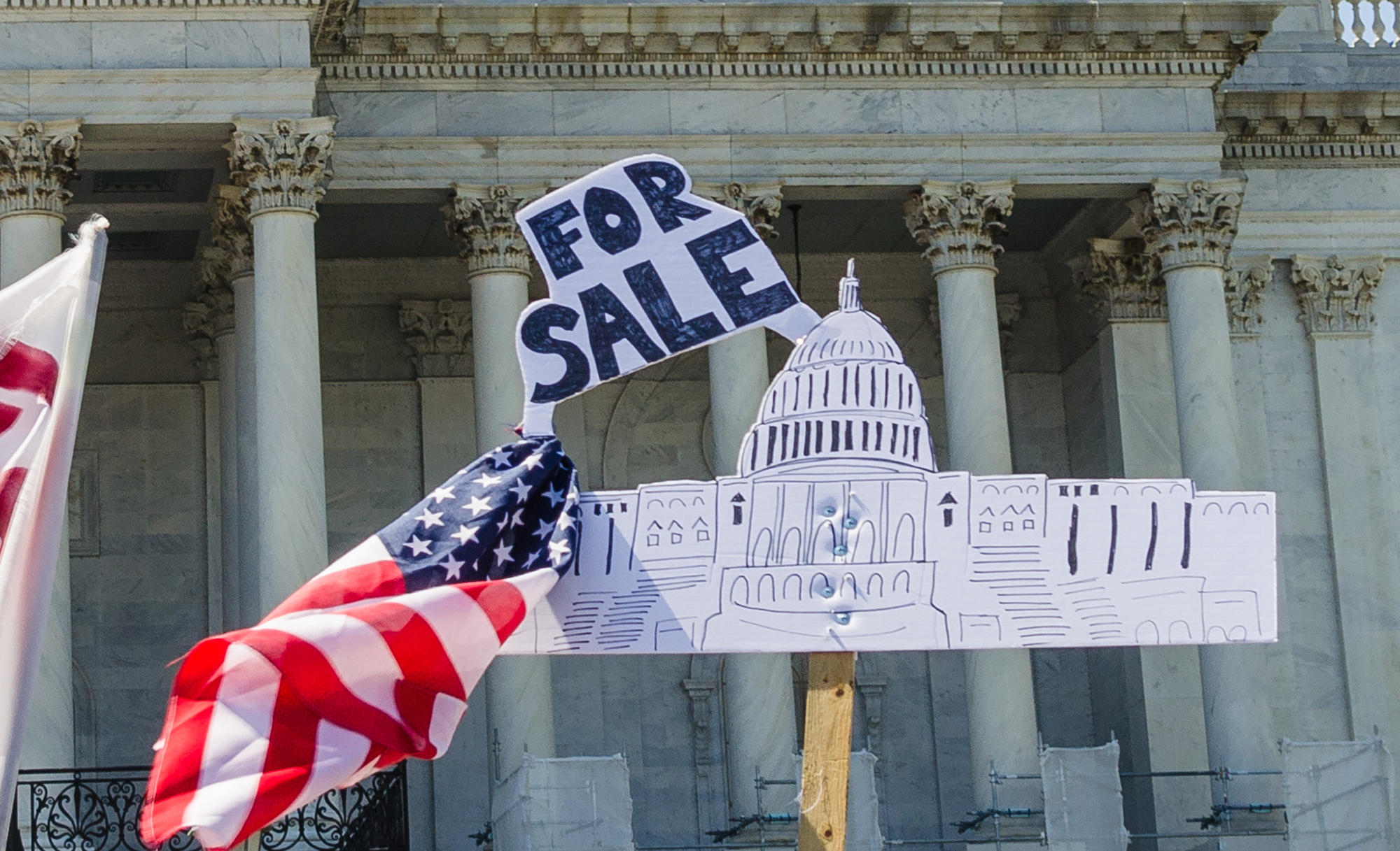 sign in front of the Capitol building with a U.S. flag that reads FOR SALE
