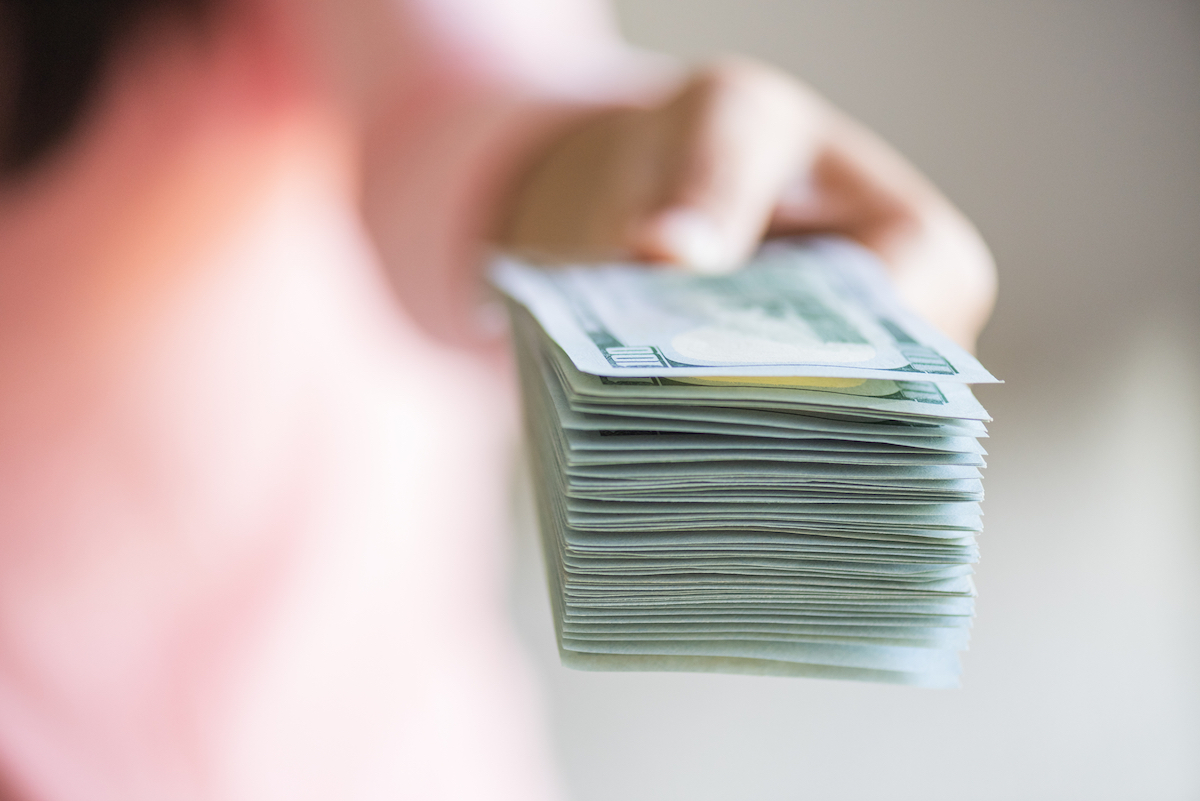 A blurred hand holding a stack of dollar bills, pushing them toward the camera. 