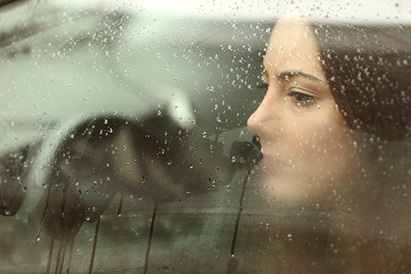 Teen driver looking out the driver’s side window of a car in the rain.