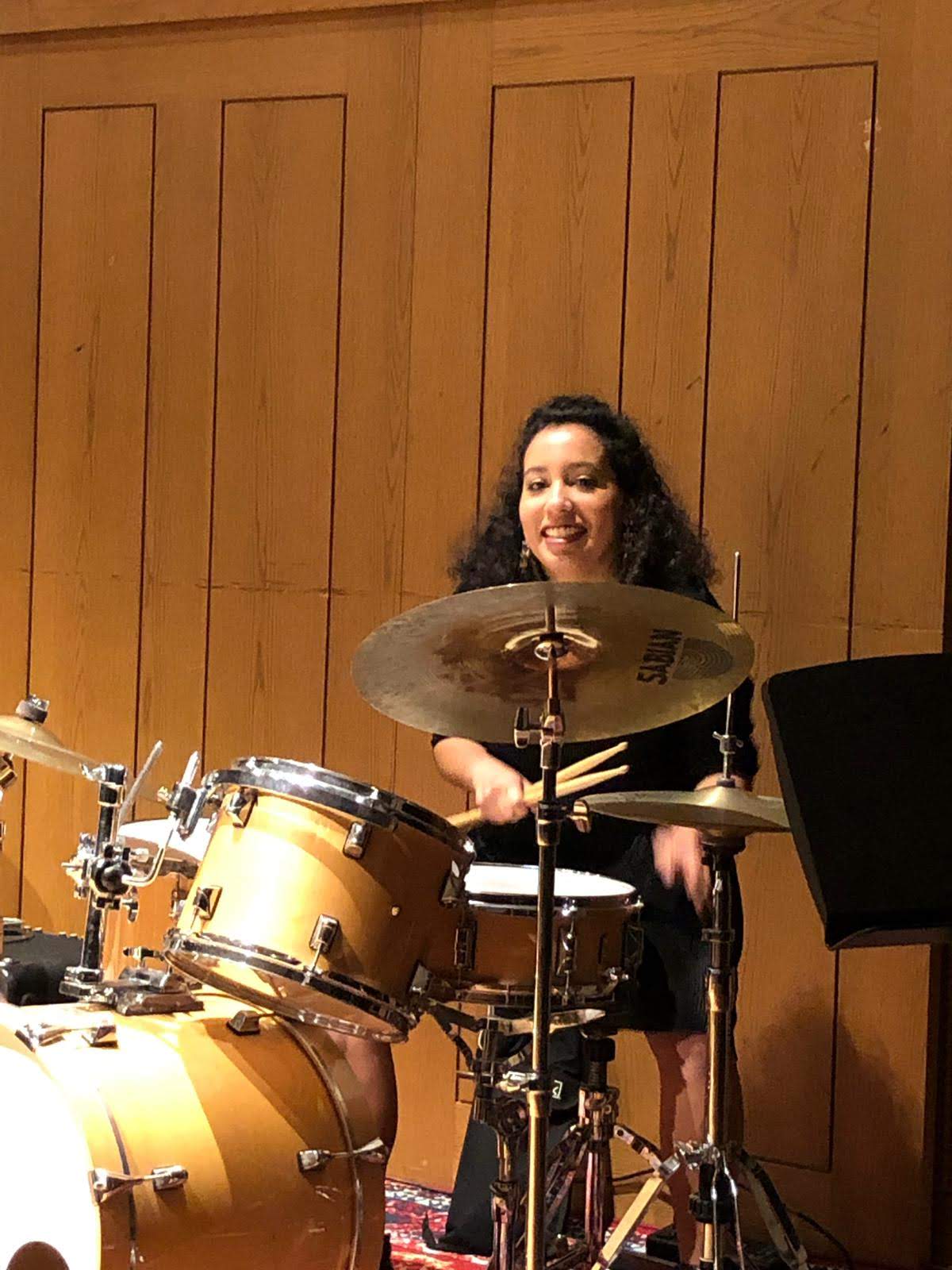 Smiling woman plays drums with wood paneling in the background