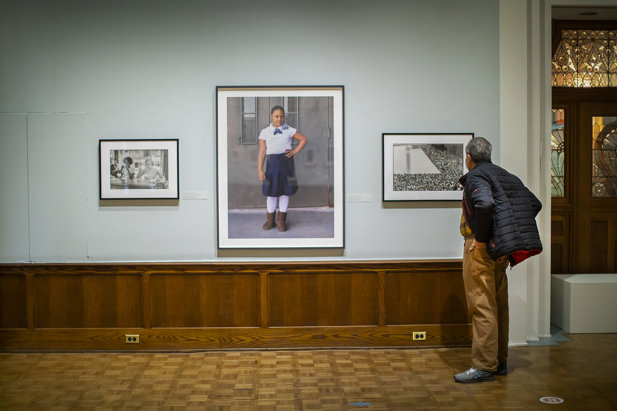 Three photographs on a wall in an art gallery with a man looking at them. 