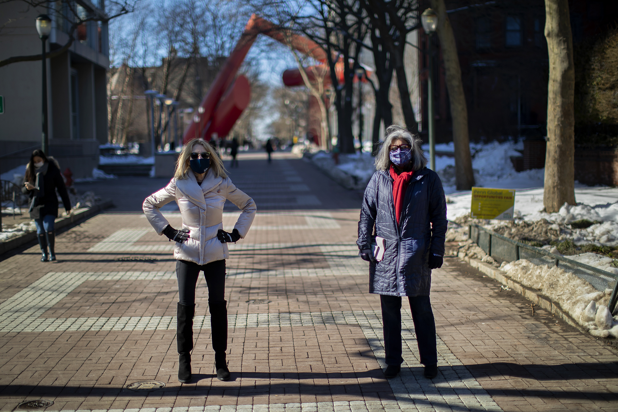 Penn President Amy Gutmann with Mamta Accapadi standing in the sunlight on Locust Walk wearing face masks.