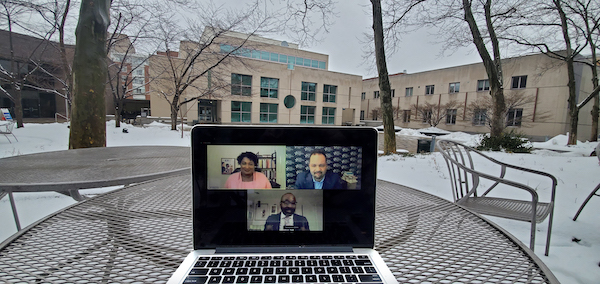 A laptop on a table outside in the snow shows three people on a Zoom call, with the Annenberg School for Communication in the background