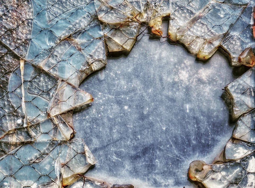 An abstract close-up image of shattered glass with different textures and colors, including grey, orange, and teal blue.