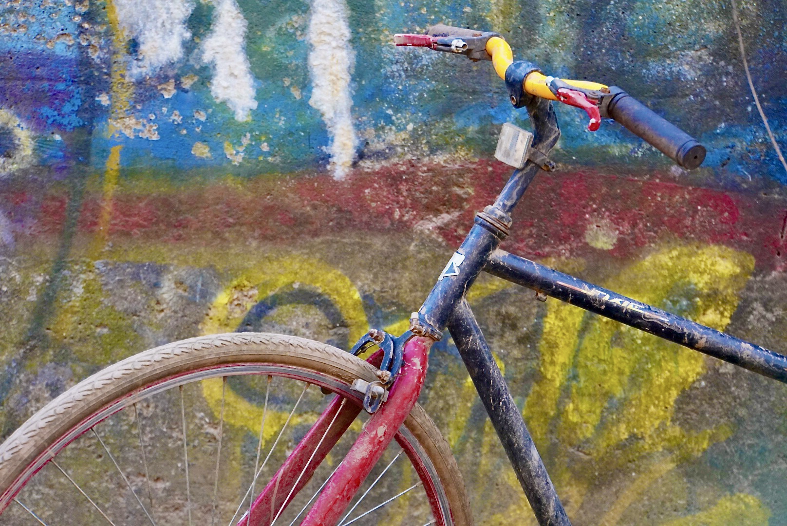 A close-up image of a bicycle leaning against a very colorful wall. 