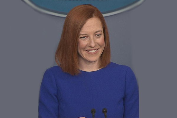 Person in a bright blue top standing at a podium with microphones, smiling. 