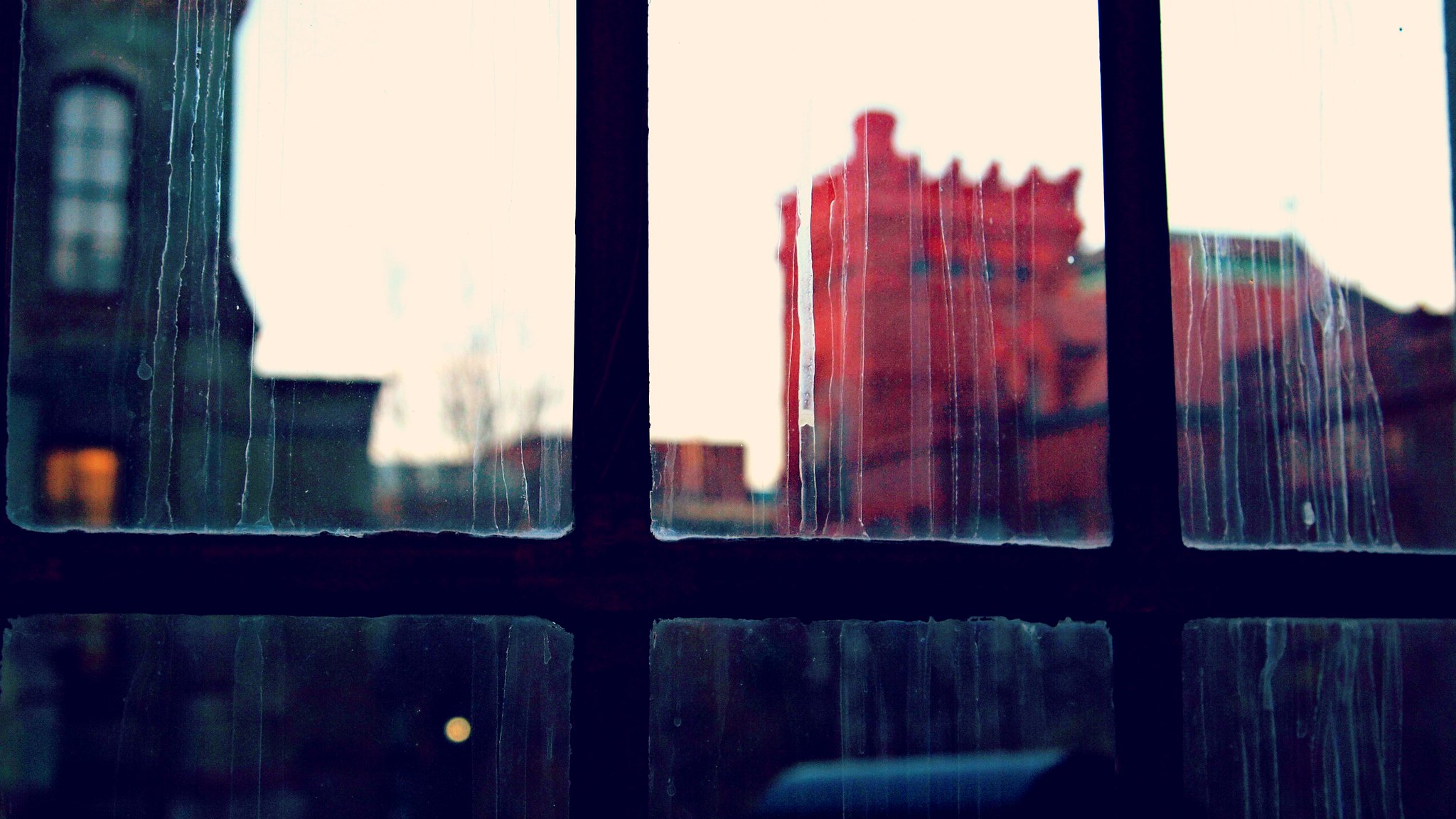 Rain streaks on a gridded window with an image of a red building behind