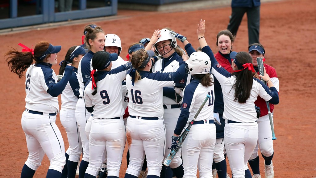 Members of the softball team celebrate in a circle at homeplate. 