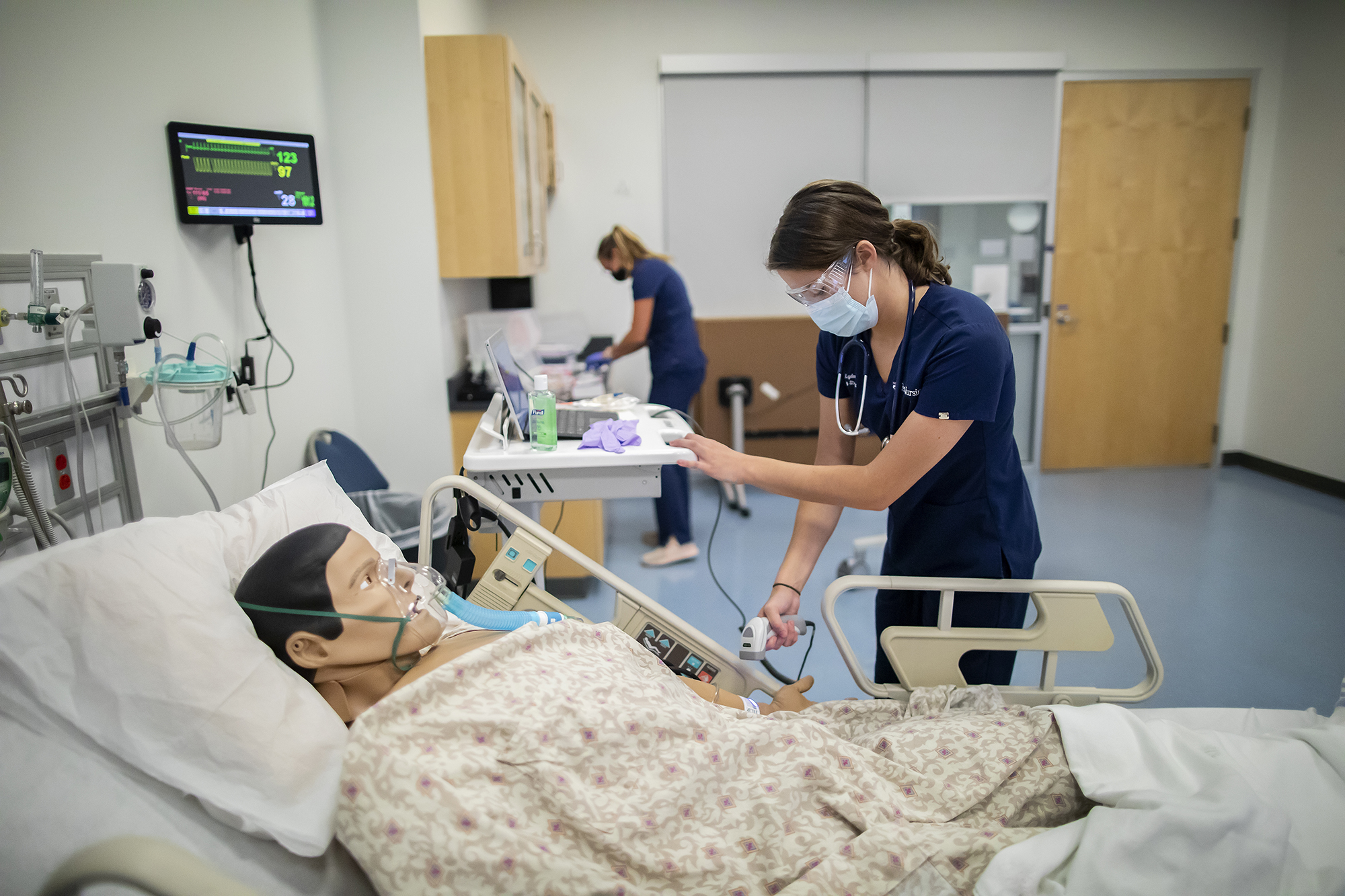 Med students wearing face masks work bedside with dummy patients during COVID.