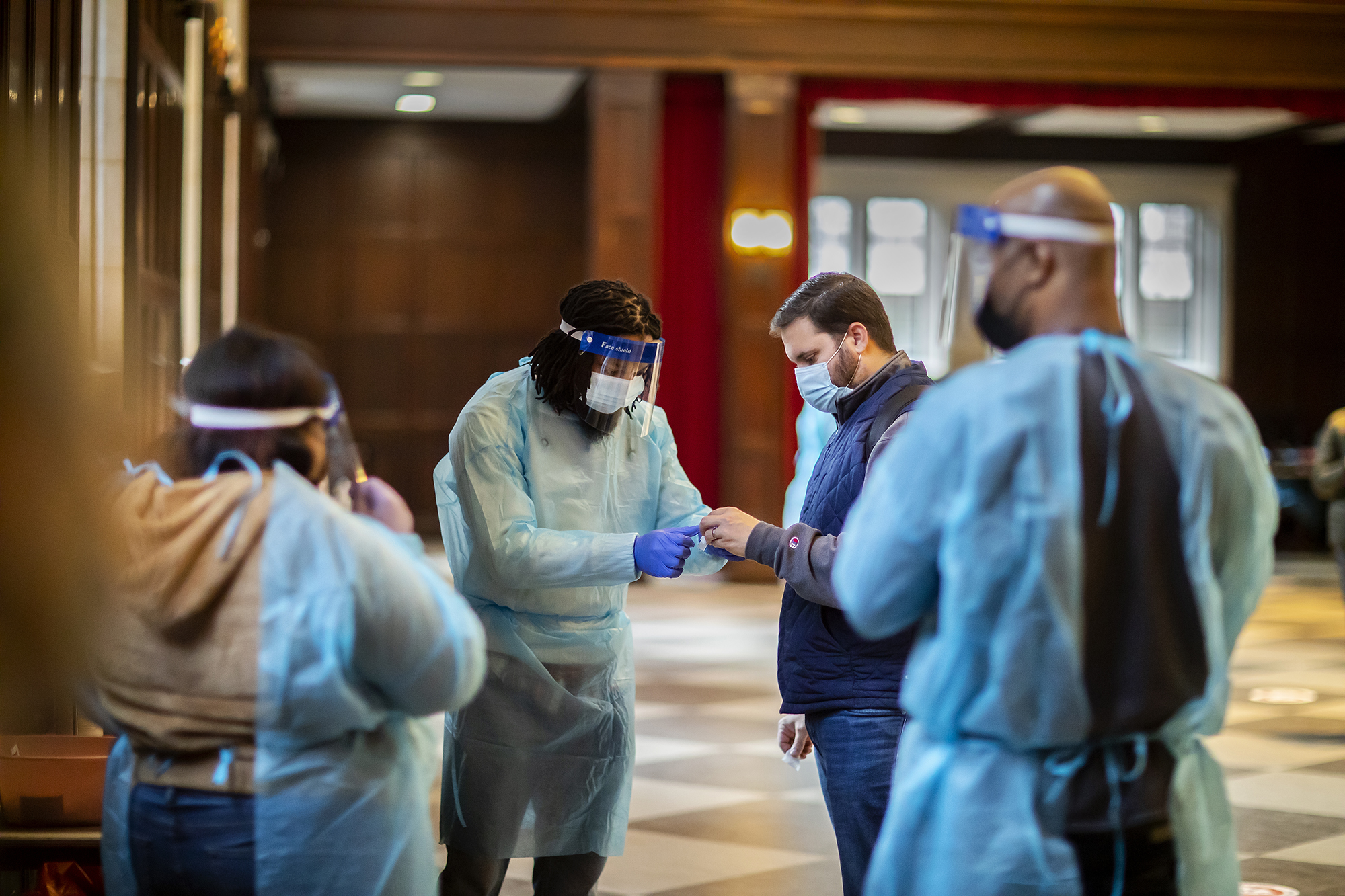 Three medical workers wearing full PPE and a fourth person wearing a face mask standing at a campus testing site. 